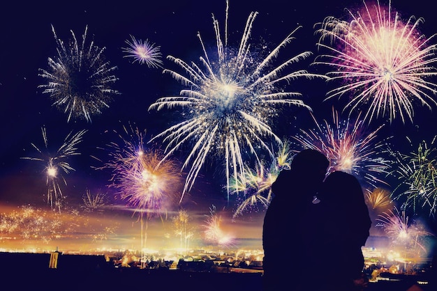 silhouette couple kissing while standing against firework display at night