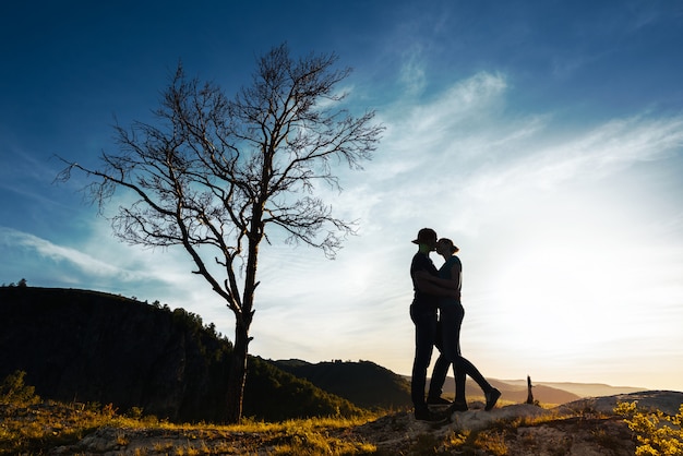 愛のカップルのシルエット。男と女の日没で抱き締めます。カップルが旅行します。自然の中の恋人。男と女が夕日を見て。日没時の恋人。山を旅します。新婚旅行