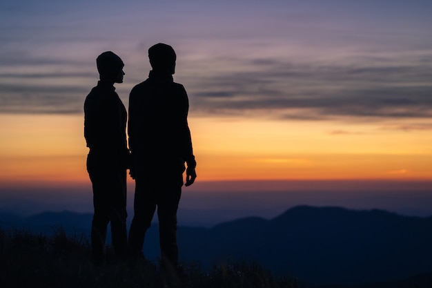 日の出を背景に山の上のカップルのシルエット