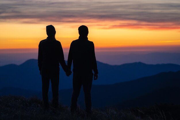 The silhouette of the couple on the mountain with a sunset background