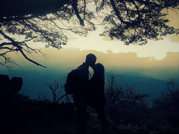 Foto una coppia di silhouette che fanno l'amore tra gli alberi sul campo al crepuscolo