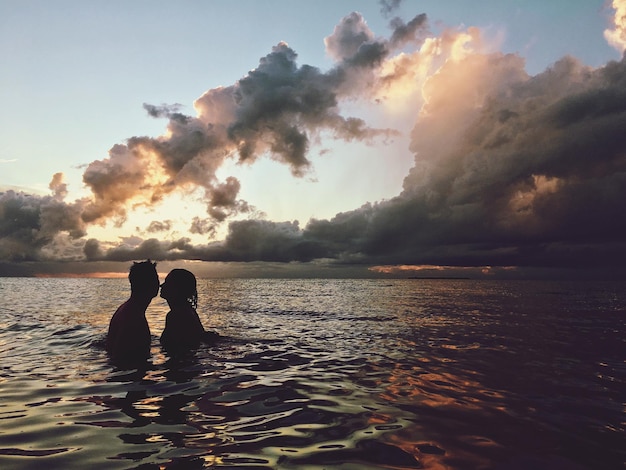 silhouette couple in sea against sky during sunset