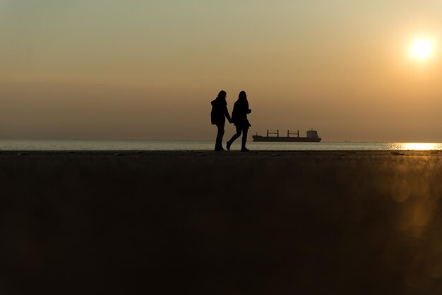 Photo silhouette couple standing on beach against sky during sunset