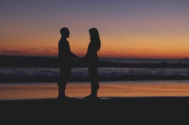 silhouette couple standing at beach during sunset