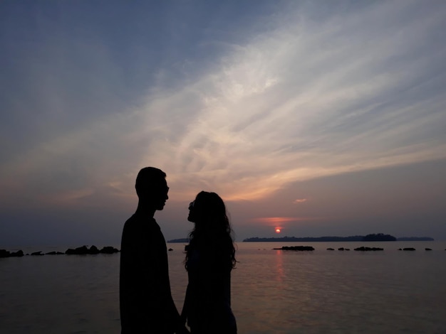 Silhouette couple standing by sea against sky during sunset