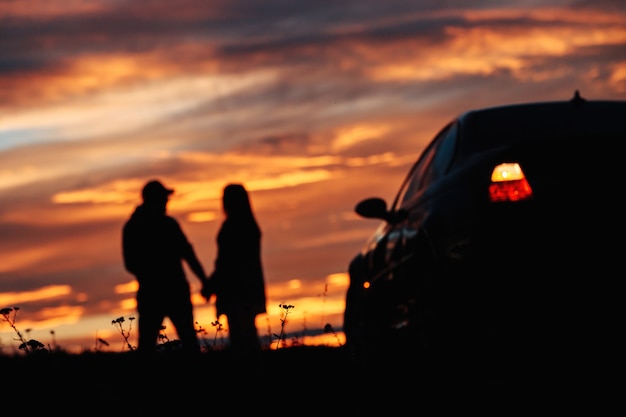 A silhouette of a couple standing near a car against the backdrop of a beautiful sunset or dawn sky.