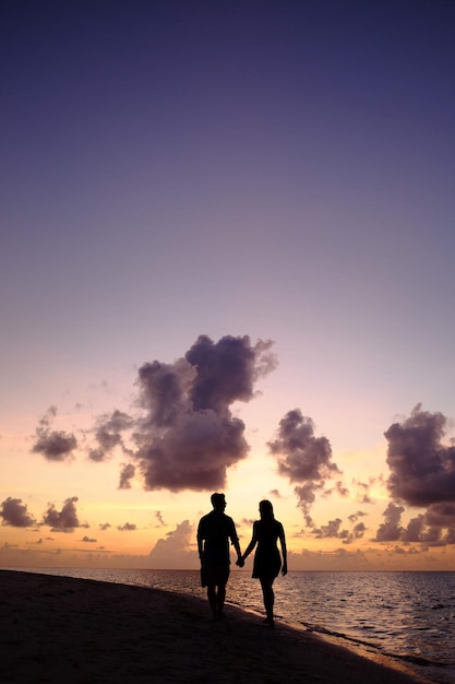 silhouette couple walking at beach against sky during sunset