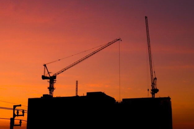 Silhouette crane by building against sky during sunset