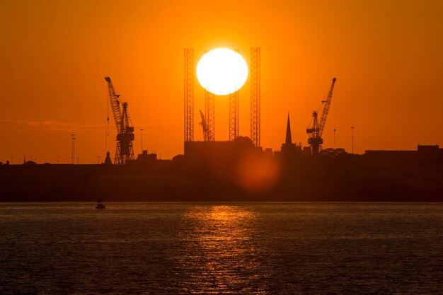 Photo silhouette cranes by river against sky during sunset at cammell laird in birkenhead