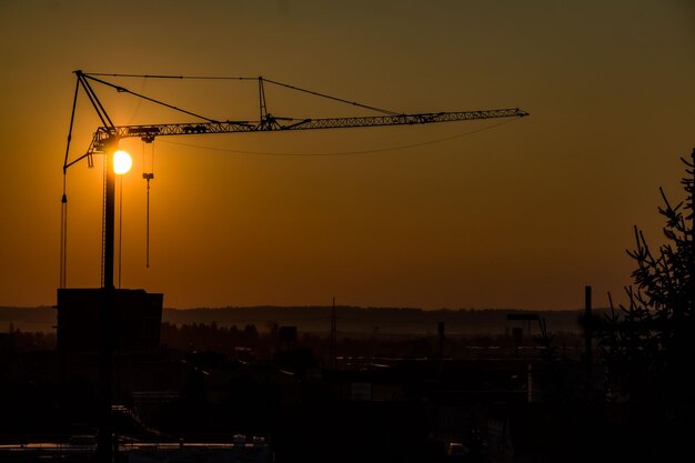 Photo silhouette cranes at construction site against sky during sunset