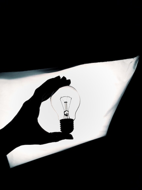 Foto silhouette mano tagliata che tiene una lampadina contro la luce illuminata