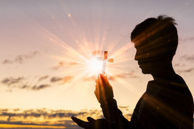 Silhouette of cross in human hand, the background is the sunrise.