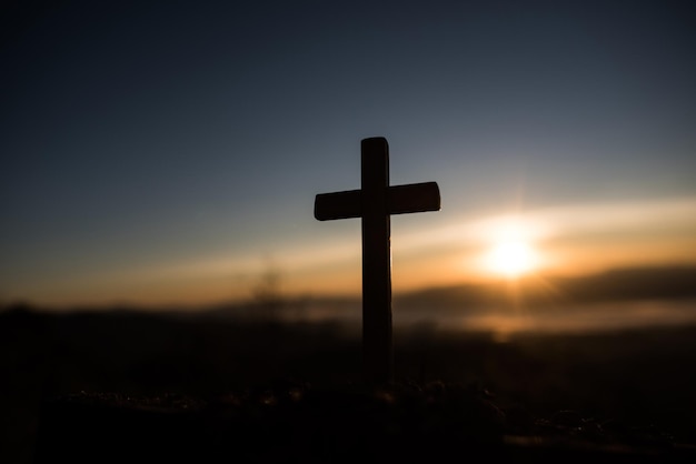 silhouette cross on land against sky during sunset