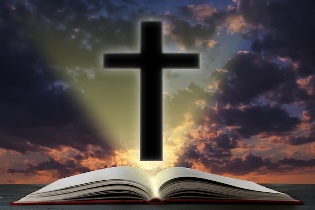 Silhouette of cross and open Bible on table against cloudy sky