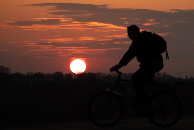 太陽と美しい空を背景にしたサイクリストのシルエット 夕日を背景に自転車に乗った男の輪郭