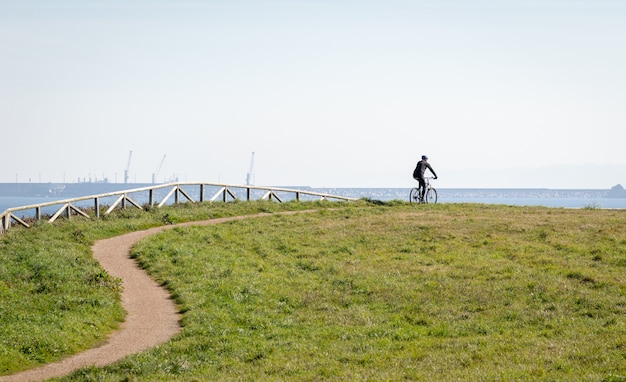 The silhouette of the cyclist a man riding on bicycle in a park with the sea at background.