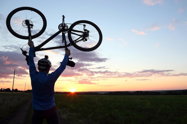 Silhouette of a cyclist with arms raised up the bike at sunset