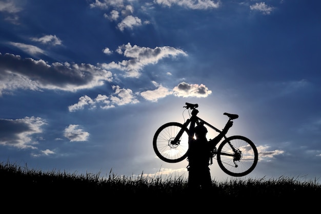 Silhouette of a cyclist with a raised bike in the grass in the sun