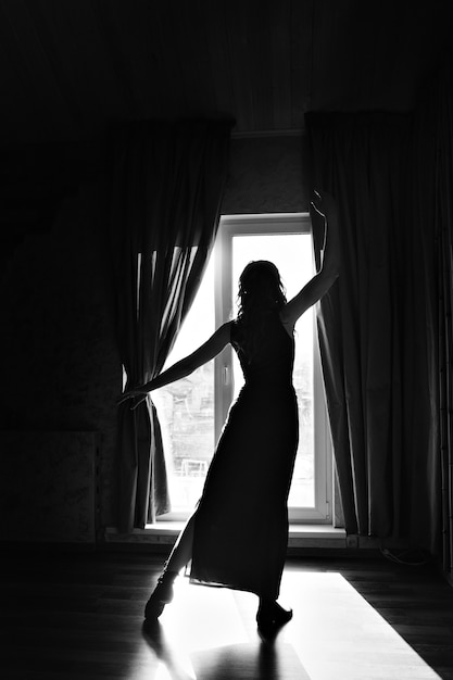 Silhouette of a dancing girl at the window. A woman in the light. The concept of strengthening the female body, grace, sport, beauty, style