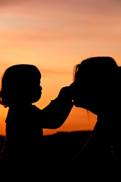 写真 オレンジ色の空を背景に母親の鼻に触れる娘のシルエット