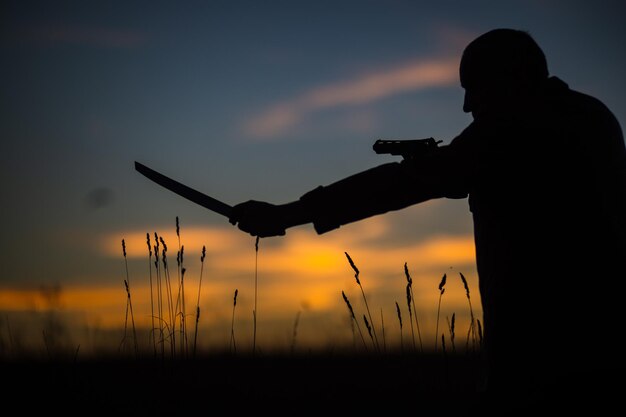 Foto silhouette di un demone e cacciatore di vampiri con un cielo drammatico sullo sfondo un uomo con una katana e un revolver concetto di fantasia e halloween