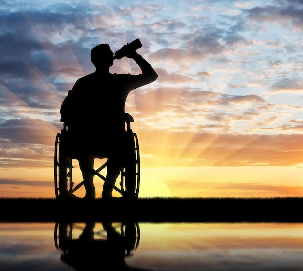 Silhouette of a disabled man in a wheelchair drinking water from a plastic bottle. Concept of leisure and recreation for disabled people