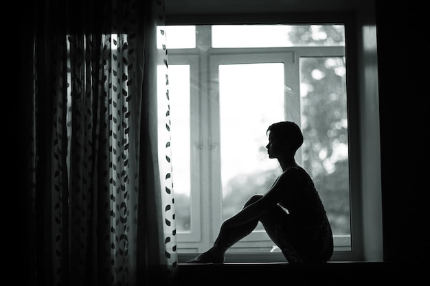 Silhouette of a dreamy girl sitting on a window