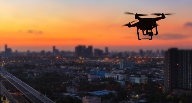 Silhouette of drone flying above city at sunset