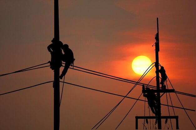 日没の空の抽象的な自然の背景とポールで遅く働くシルエット電気労働者