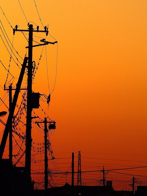 Silhouette electricity pylon against orange sky