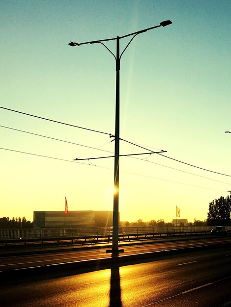 Silhouette electricity pylons against clear sky during sunset