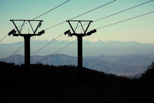 Silhouette electricity pylons by mountains against clear sky