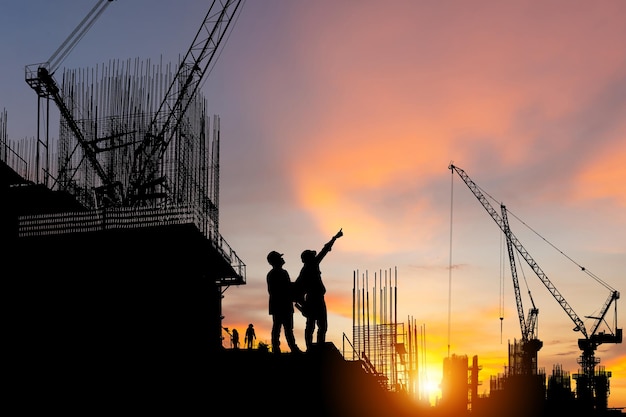 Silhouette of Engineer and worker on building site, construction site at sunset in evening time.