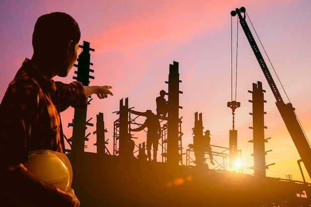 Foto silhouette di ingegnere e lavoratore sul cantiere edile con il tramonto la sera come sfondo