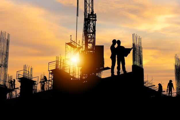 Silhouette di ingegnere e squadra di lavoratori in cantiere, cantiere con tramonto in serata