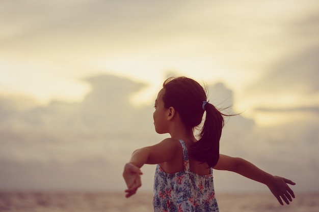 ビーチで小さな女の子を楽しむシルエット、屋外の夏の夕焼け空でリラックスする子供