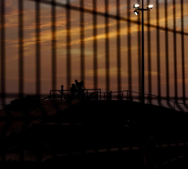 Photo silhouette family at skateboard park seen through fence against sky during sunset