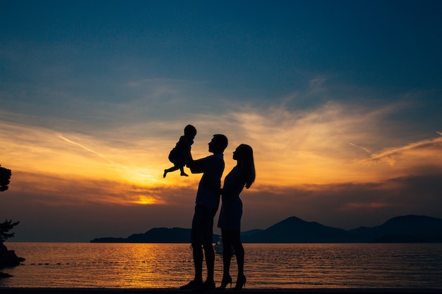 Silhouette of a family with children against the backdrop of the setting sun and sea