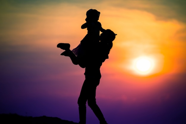 Silhouette of a family with a happy mother playing with a girl in the sunset sky