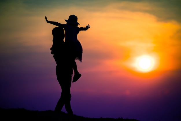 Foto silhouette di una famiglia con una madre felice che gioca con una ragazza nel cielo al tramonto