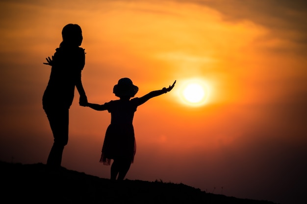 Silhouette di una famiglia con una madre felice che gioca con una ragazza nel cielo al tramonto