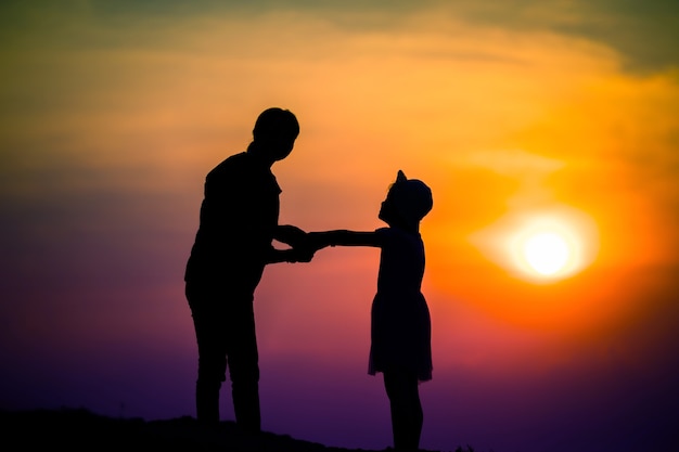 Silhouette of a family with a happy mother playing with a girl in the sunset sky