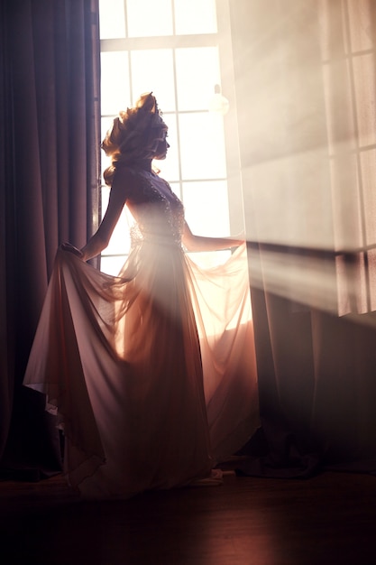 太陽の下で窓の近くのシルエットファッション女性。
