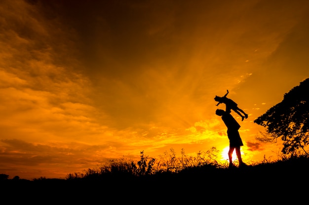 Silhouette of father and daugther on a mound at sunset. 