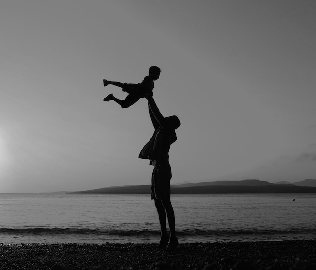 Foto silhouette padre che solleva il figlio sulla spiaggia contro il cielo