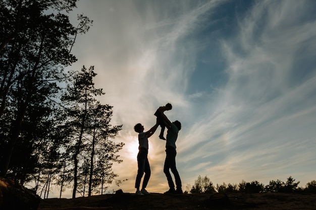 The silhouette of a father and mother raising their son above them against the background of the sunset