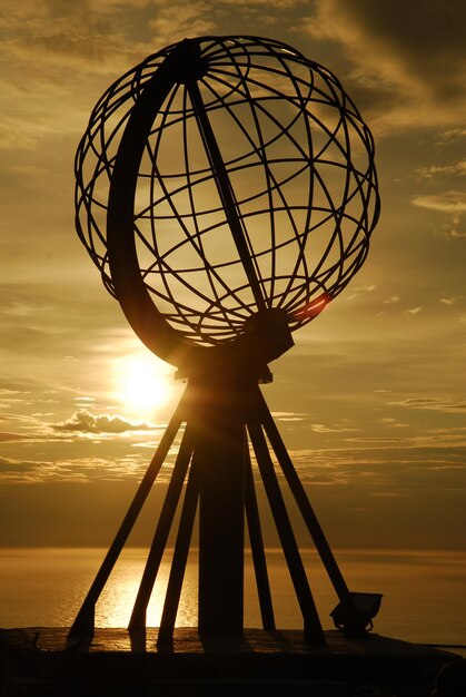 Silhouette ferris wheel against sea during sunset