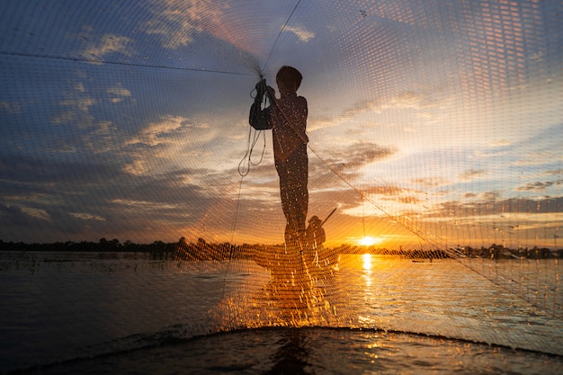 Siluetta del pescatore sul peschereccio con rete sul lago al tramonto, tailandia