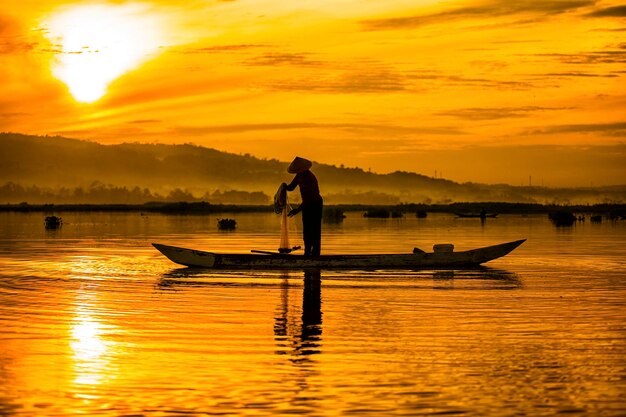 Silhouette fisherman fishing at lake against orange sky