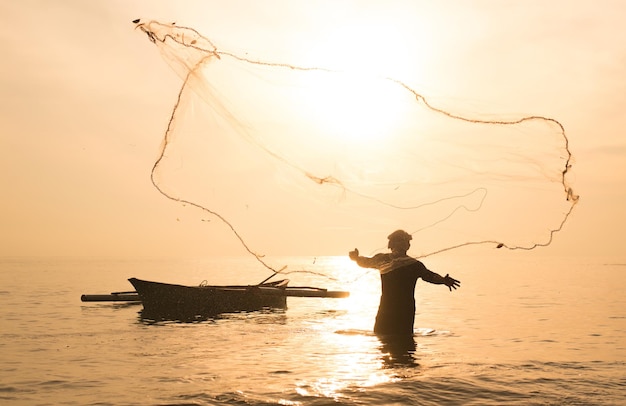 silhouette fisherman fishing in sea against orange sky